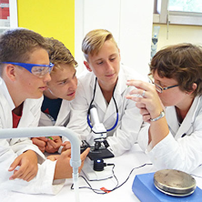 Teens - 5. bis 8. Schulstufe=Drei Schüler lauschen einer Laborkraft